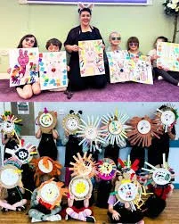 Children and adults holding up colorful handcrafted arts and crafts, including decorated paper plates and posters in a classroom setting.