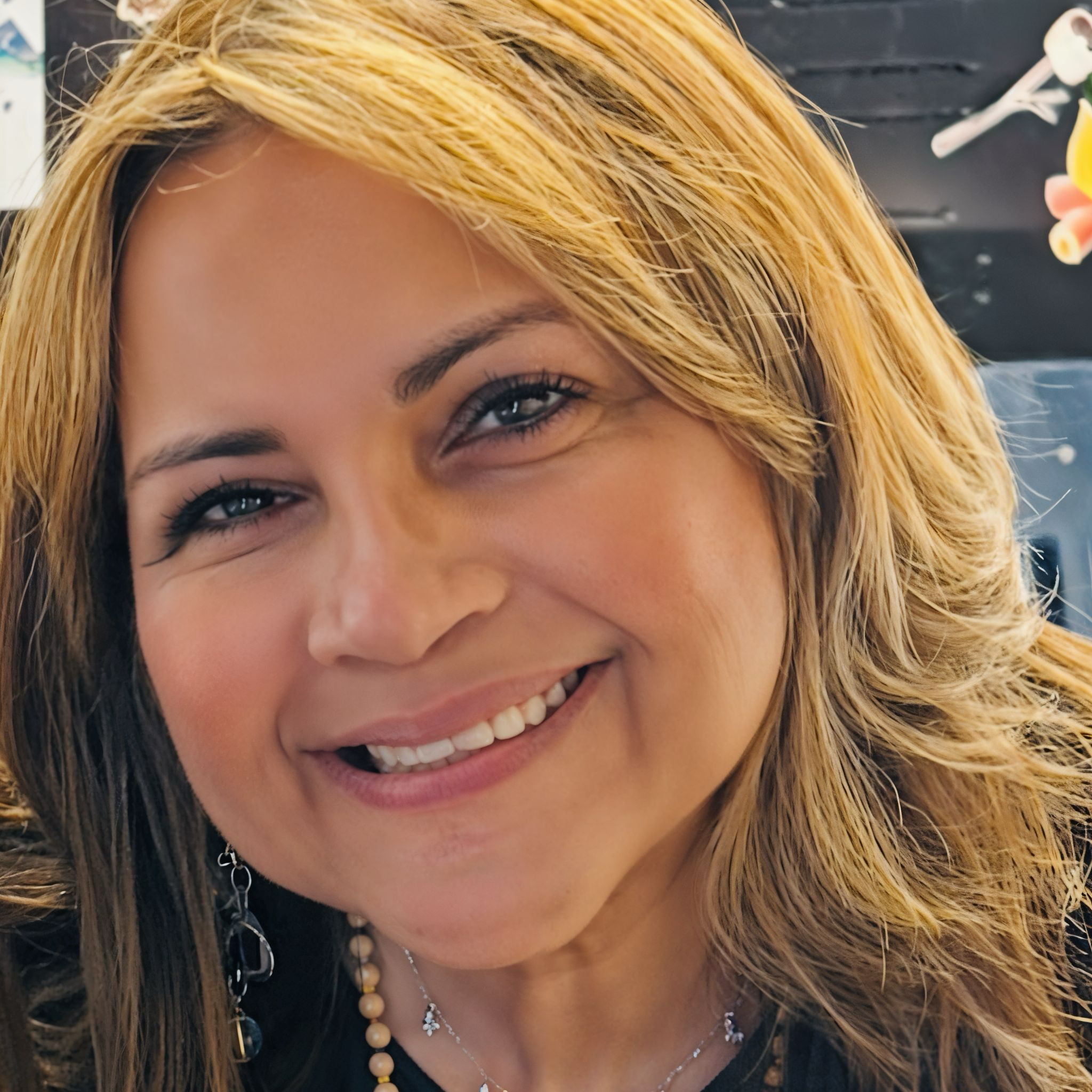 Close-up of a smiling woman with blonde hair, wearing earrings and a necklace.