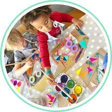 Children painting and crafting at a table with various art supplies, including paints, brushes, and paper.