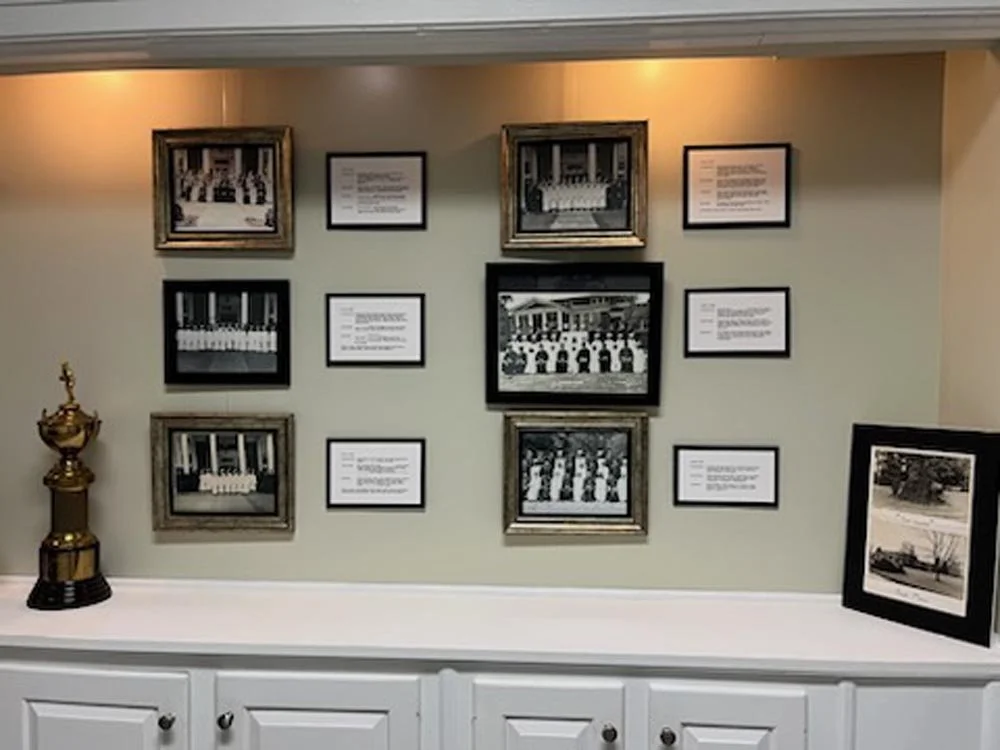Wall display with framed historical photos and descriptions, a trophy on a white cabinet, and a framed landscape photo on the right.