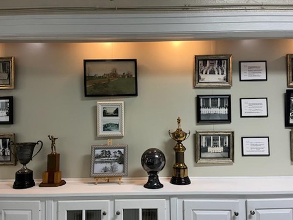 A display wall with framed photographs and plaques, trophies, and a globe on a white cabinet.