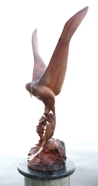 Wooden sculpture of a bird with wings spread, perched on a rock base.
