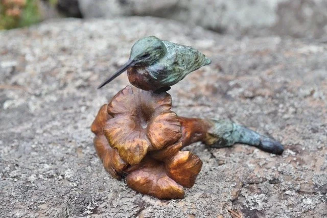 A small metal sculpture of a bird perched on a mushroom, placed on a rocky surface.