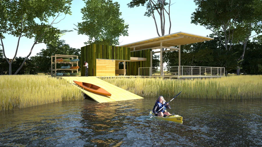 Person kayaking in a river near a modern wooden building with a ramp and outdoor seating, surrounded by trees and grassy area.