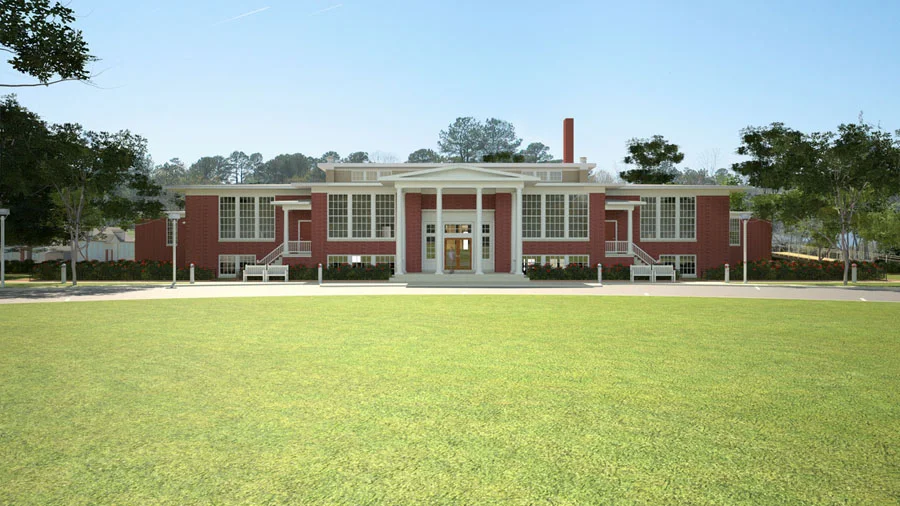A large red brick building with white architectural details, surrounded by a well-maintained lawn and trees, and set against a clear blue sky.