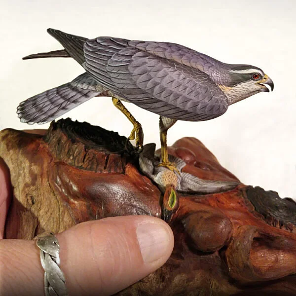 A detailed model of a bird of prey, possibly a falcon, perched on a wooden base that resembles a tree trunk.