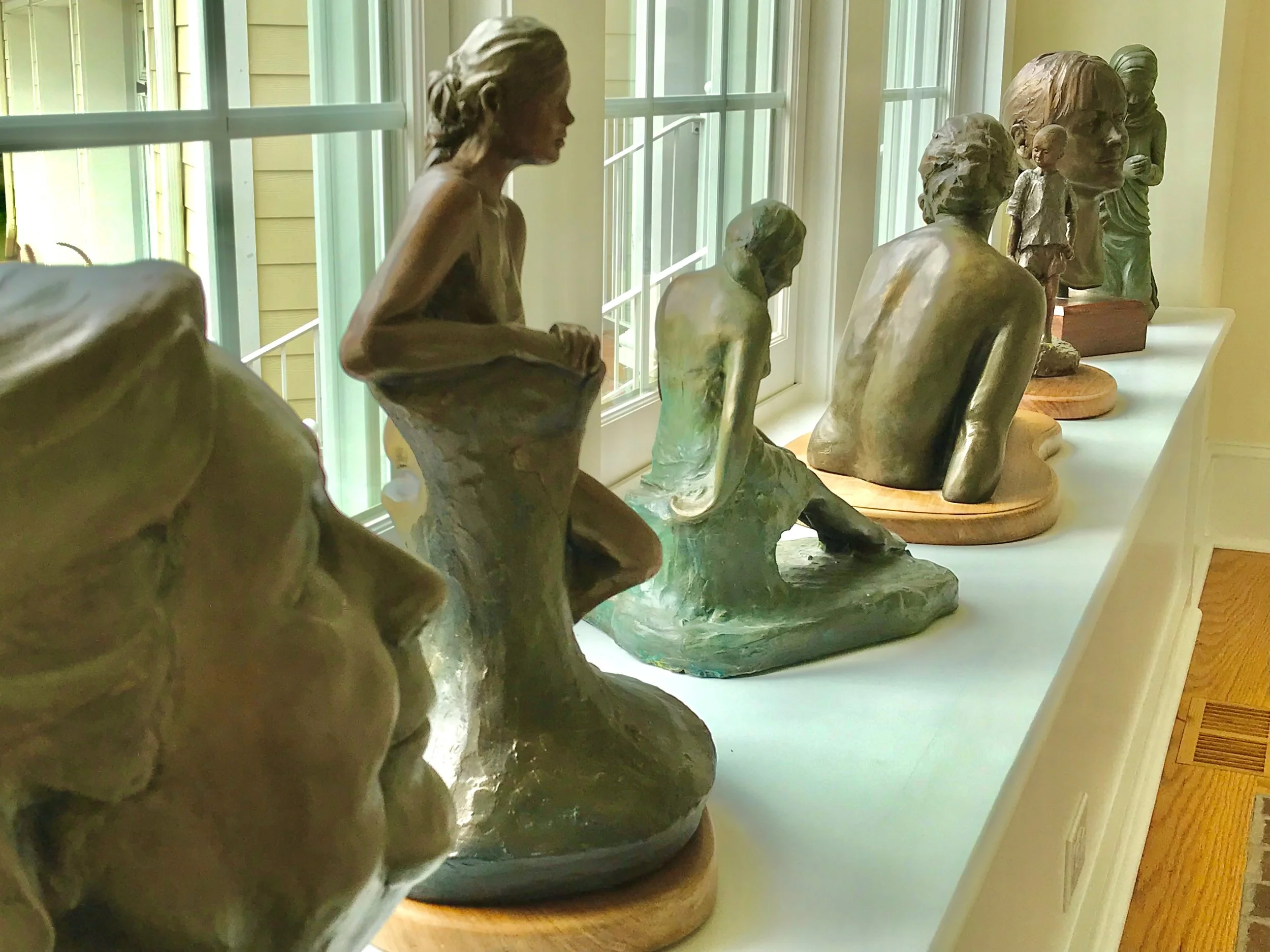 Art sculptures of human figures displayed on a windowsill inside a room with yellow walls and large windows.