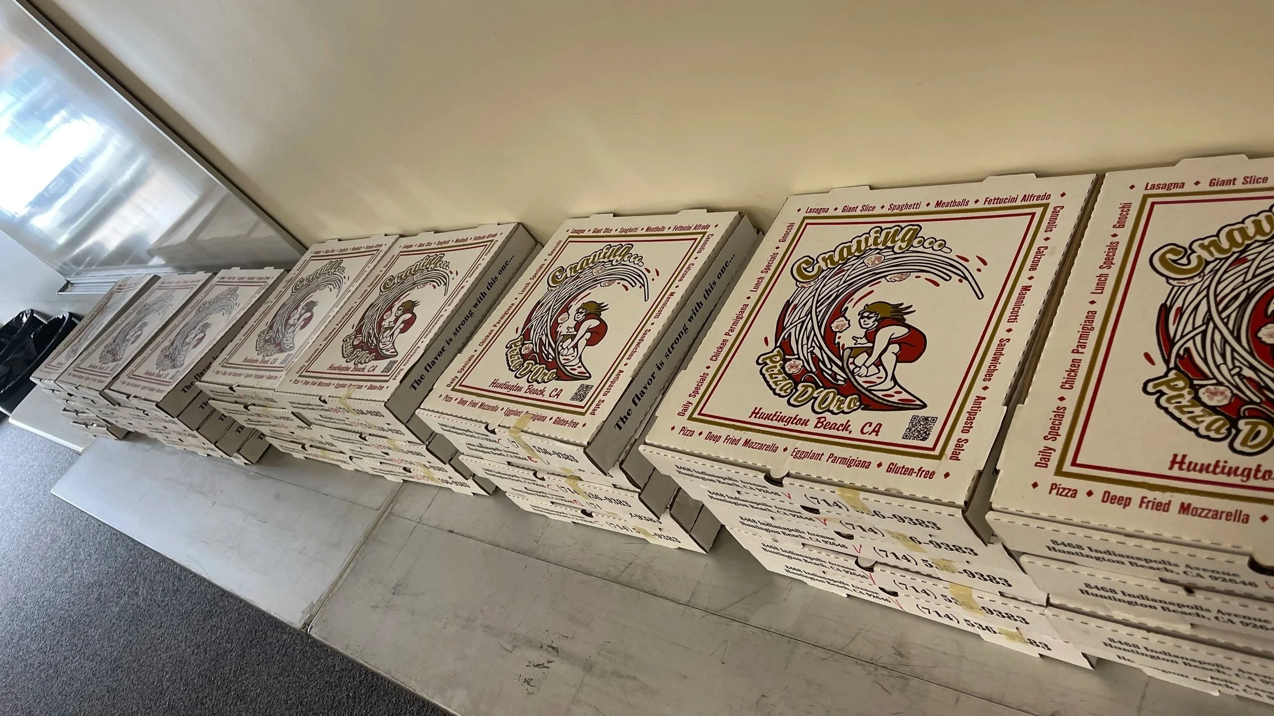 Stacked pizza boxes on a table, labeled with the restaurant name 'Pasta D'Oro' and featuring a cartoon of a woman with long hair. The boxes list various Italian dishes like lasagna, spaghetti, and pizza.