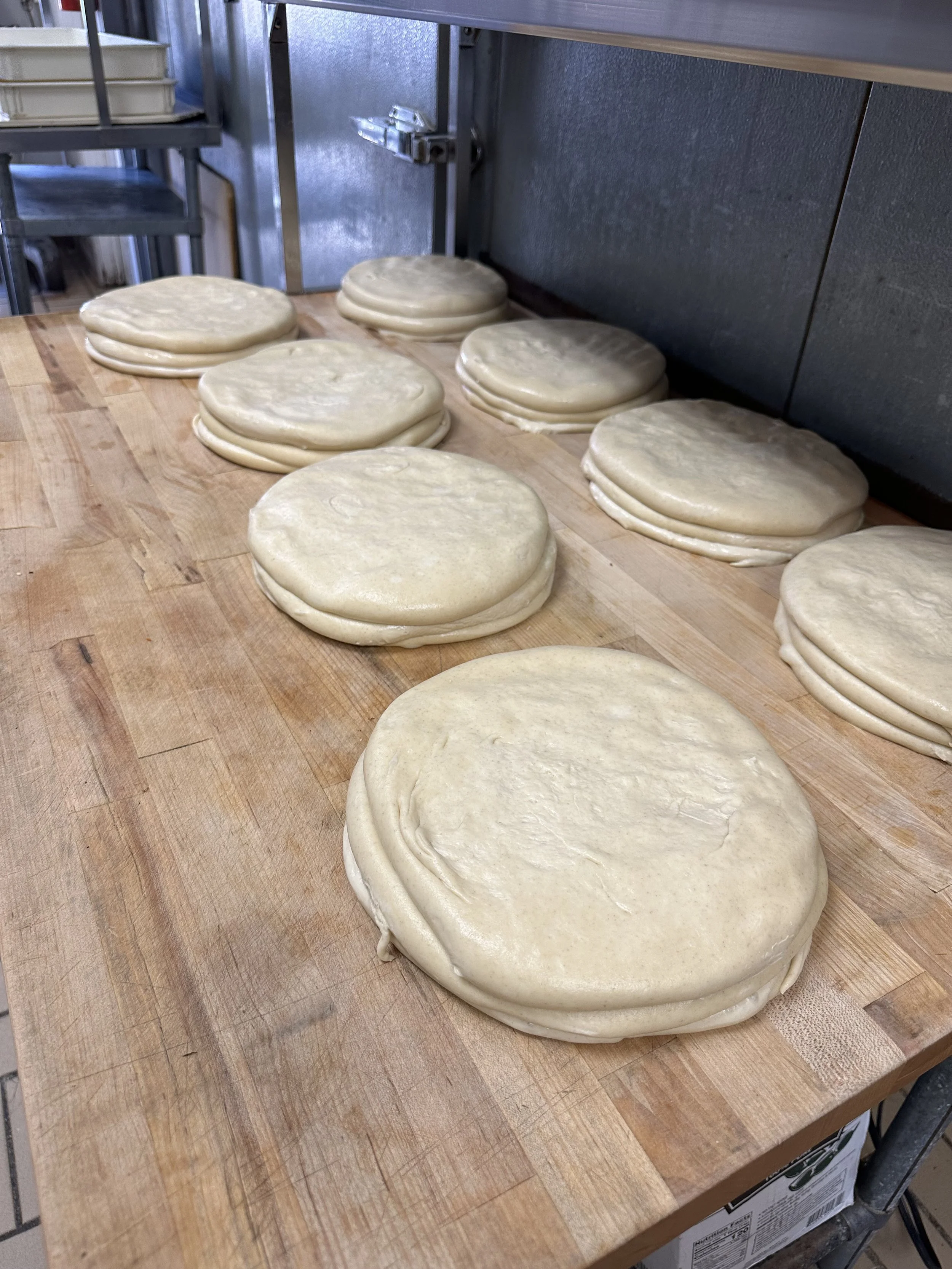 Piles of round dough discs on a wooden work surface, ready for baking or cooking.
