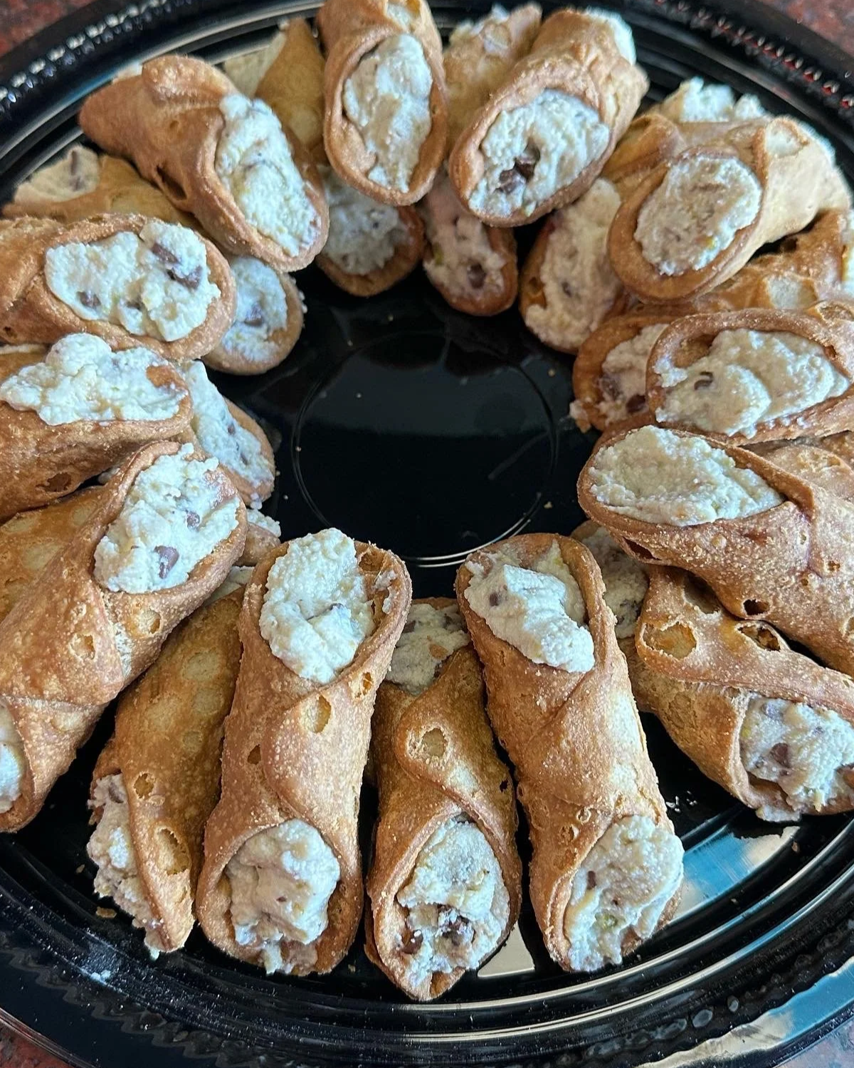 Cannoli with crispy shells filled with creamy cheese and chocolate chips on a black platter.