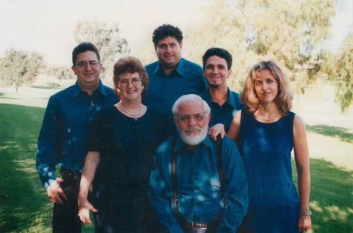 The DiPietro family, smiling together outdoors on a grassy area with trees in the background, dressed in blue clothing.