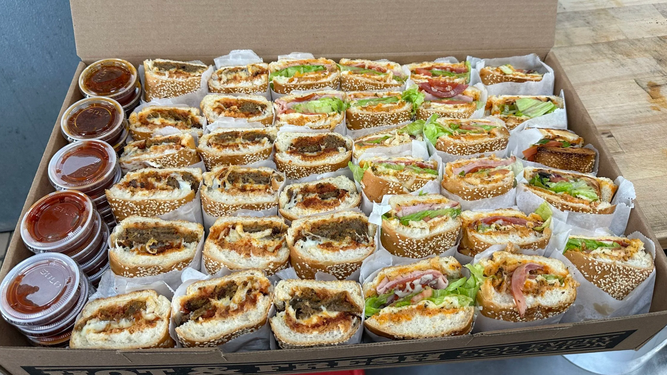 A box filled with assorted sandwiches and small containers of dipping sauces.