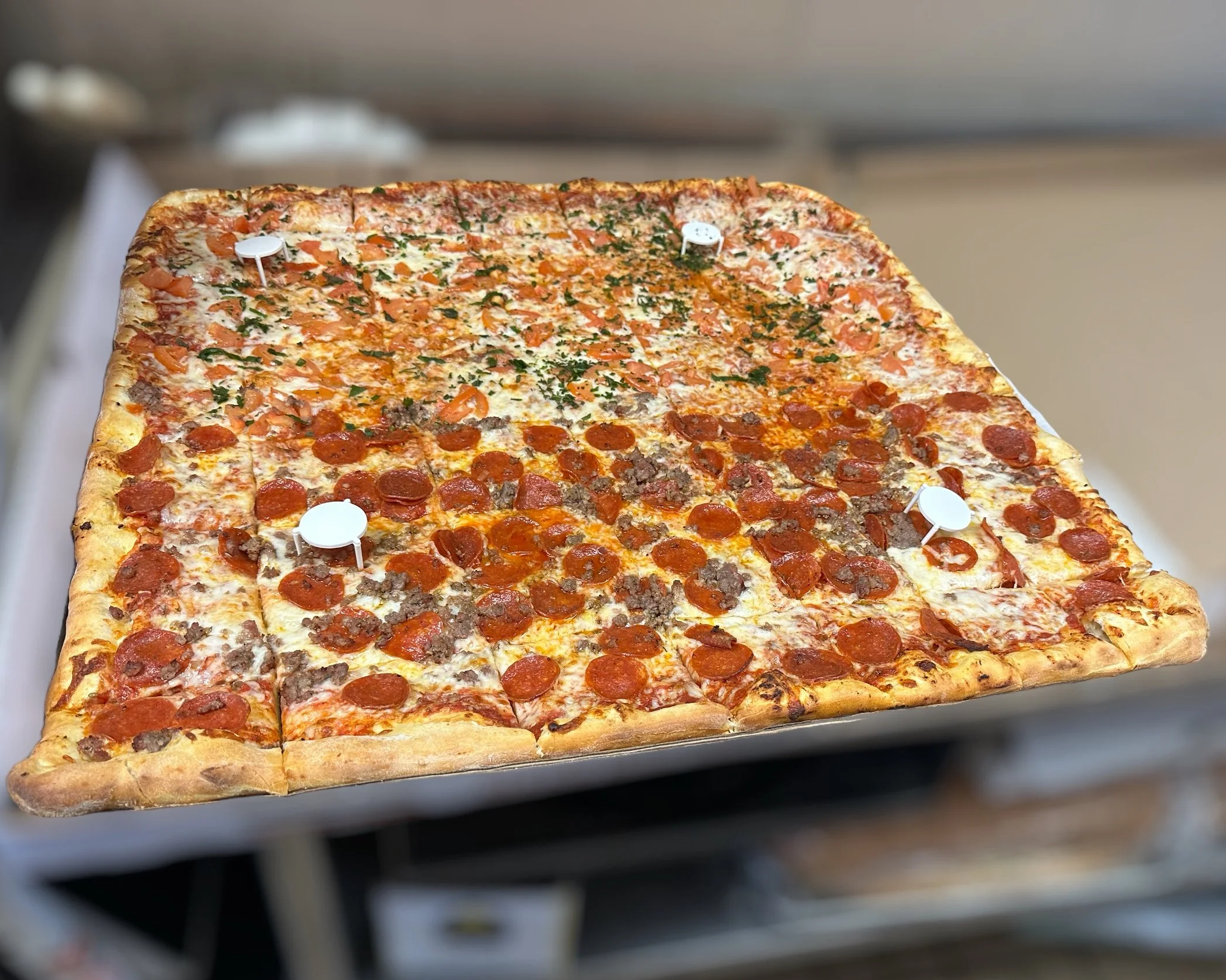 Square 28" party pizza with pepperoni, sausage, and chopped herbs on top.