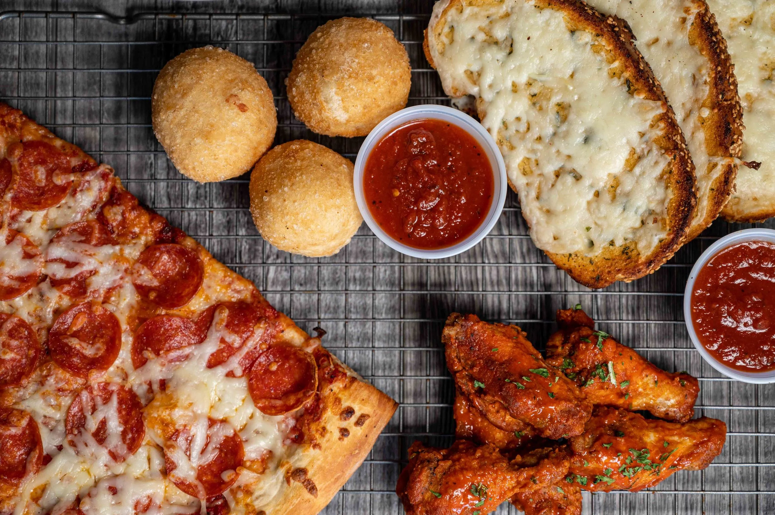 Assorted slices of pizza and fried snacks with dipping sauces on a wire rack.