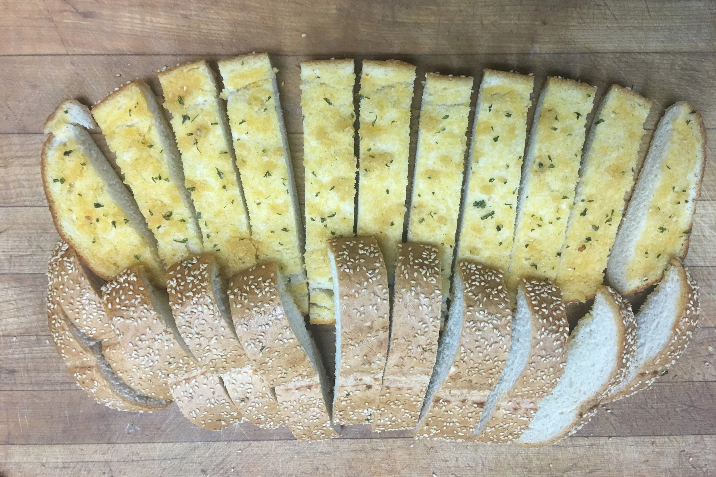 Sliced yellow cornbread and sesame seed buns arranged on a wooden cutting board.
