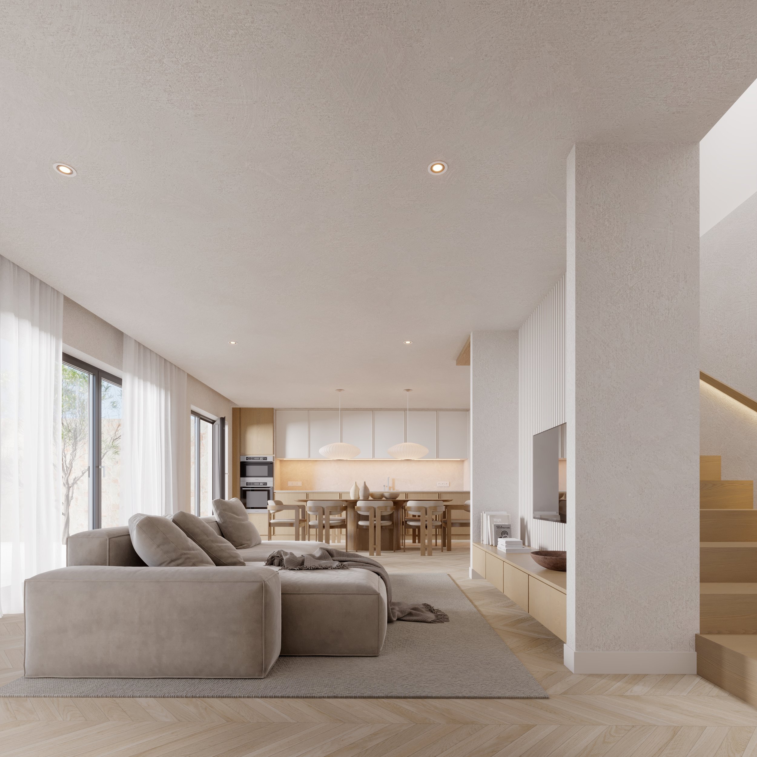 Modern open concept living room with beige sectional sofa, light wood flooring, white walls, sliding glass doors with white curtains, and a kitchen with a central island and pendant lights in the background.