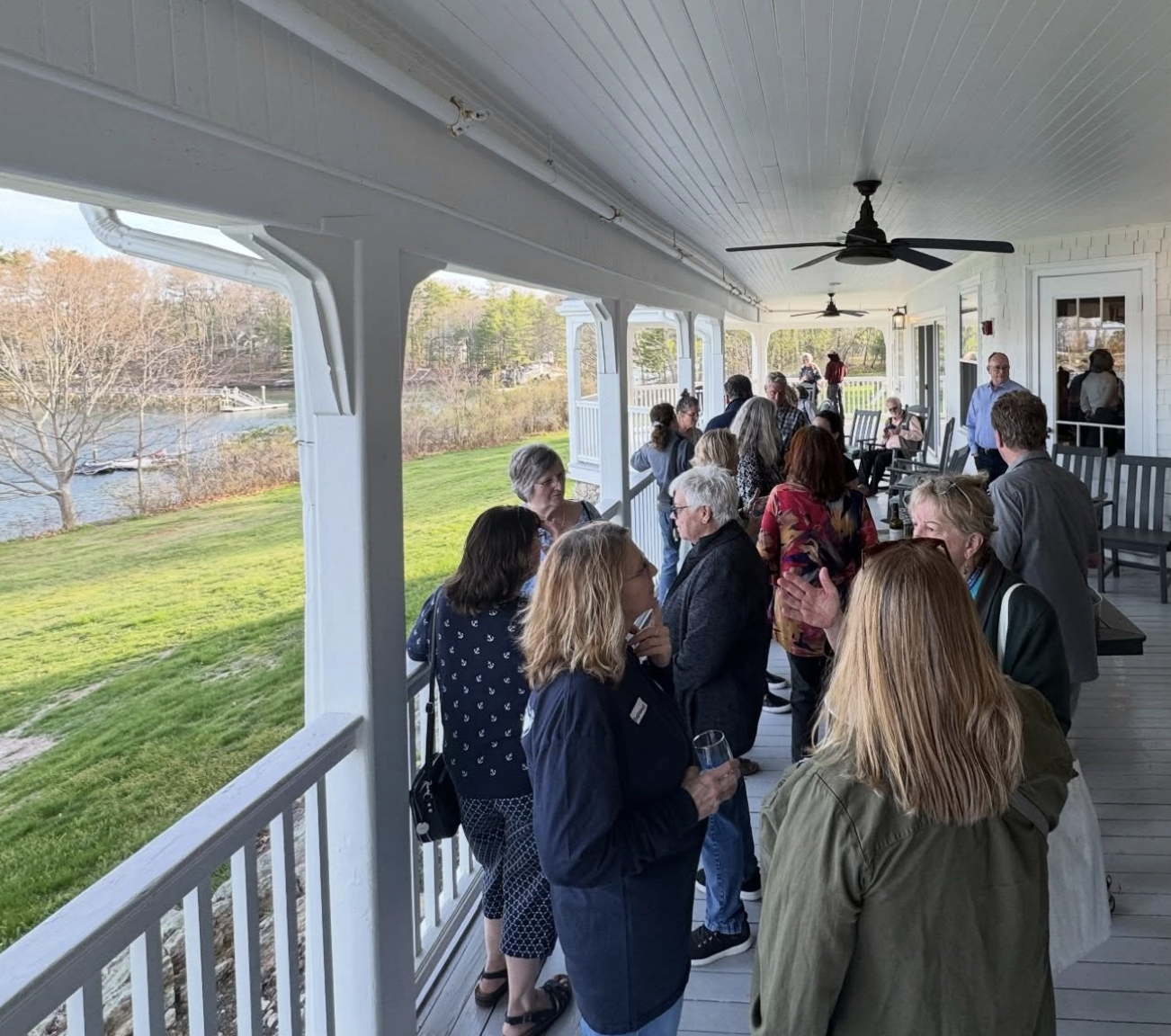 People gathered on a porch overlooking a river during an outdoor social event.