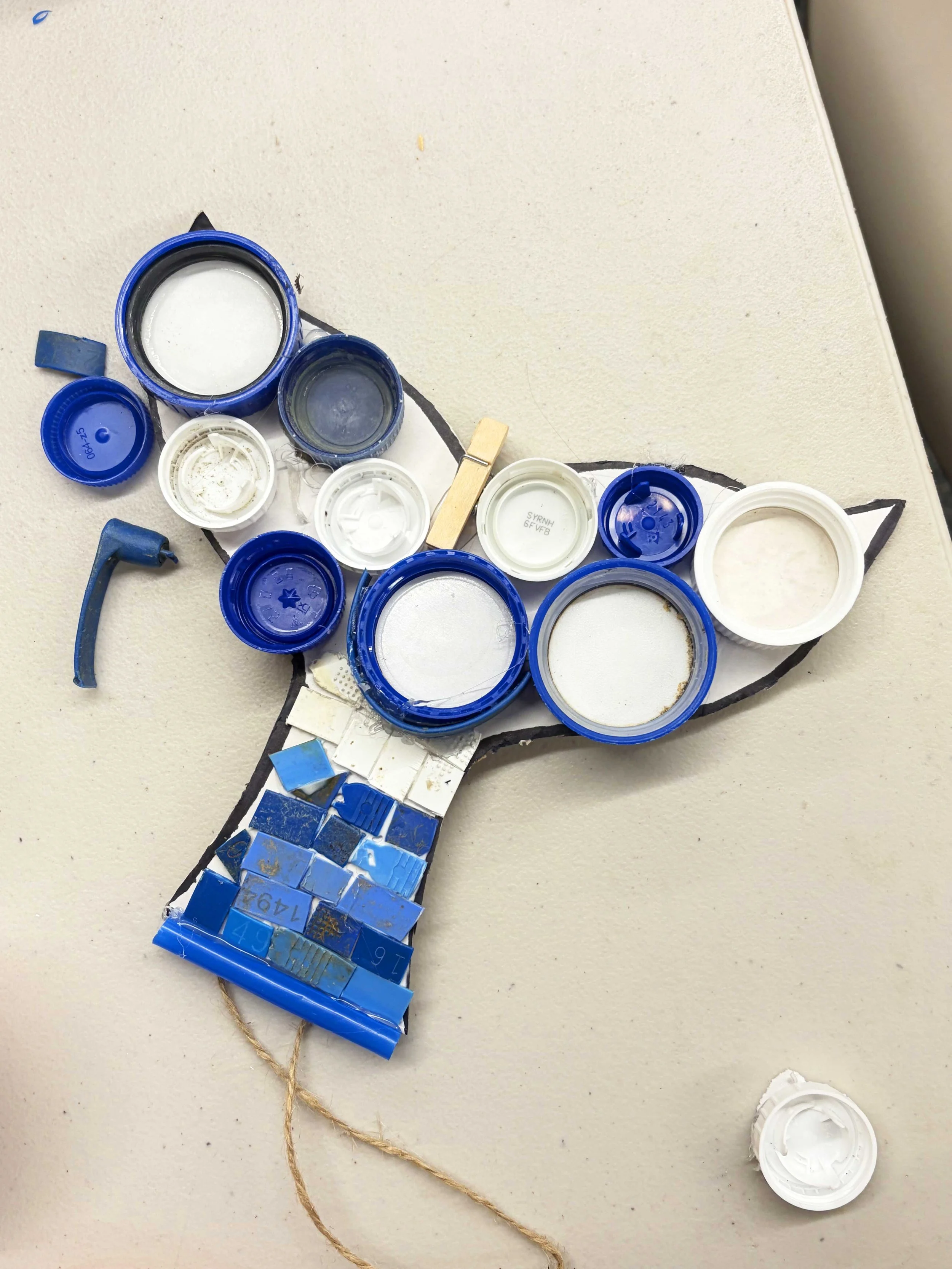 Various blue and white plastic bottle caps arranged on a beige surface, some attached with a piece of string or twine