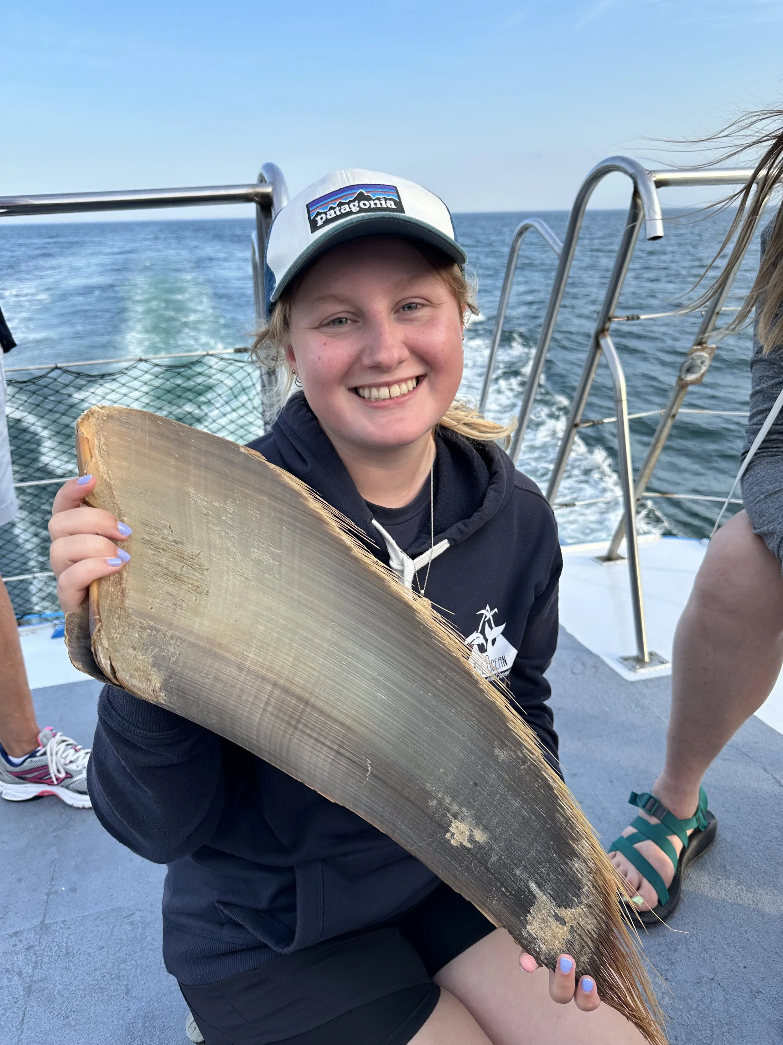 Woman sitting on a boat holding a large fish she caught, with the ocean and sky in the background.