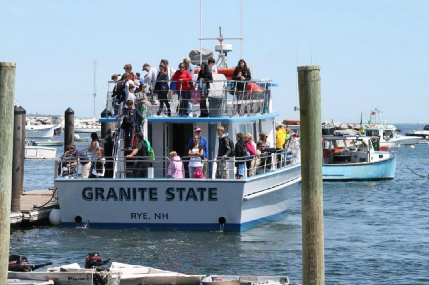 Tourist boat named 'Granite State' docked at a marina with people boarding and disembarking, surrounded by other boats and blue sky.