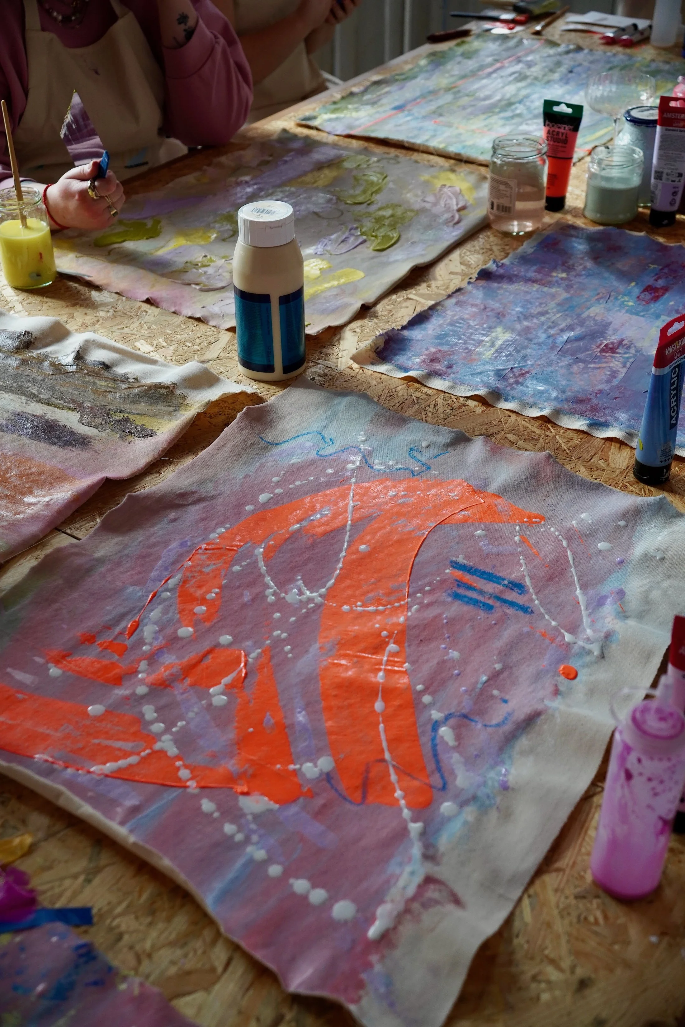 Bunte abstrakte Kunstwerke auf Papieren, die auf einem Tisch liegen, mit verschiedenen Farben, Pinsel und Farbtuben zum Malen.