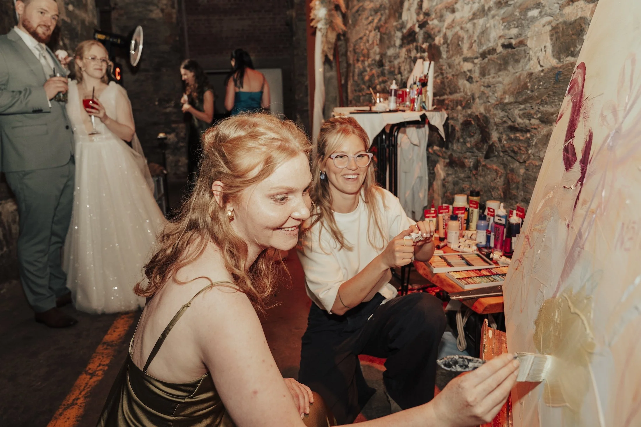 Frauen beim Malen in einer Kunstgalerie, mit vielen Farben und Pinseln auf einem Tisch.