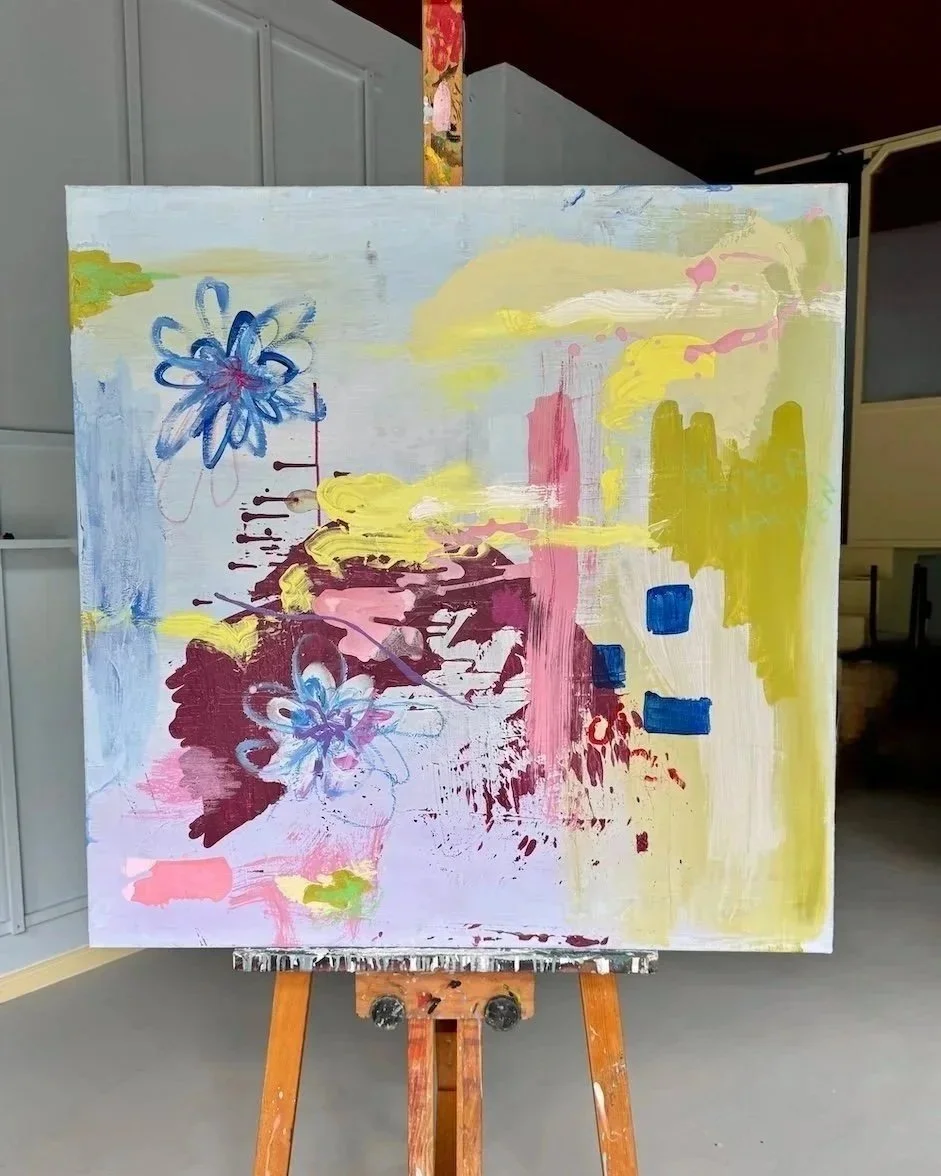 Abstraktes gemaltes Bild auf Leinwand mit blauen, gelben, rosa und weißen Farbklecksen und -strichen. Das Gemälde ist auf einem Holzständer aufgestellt.