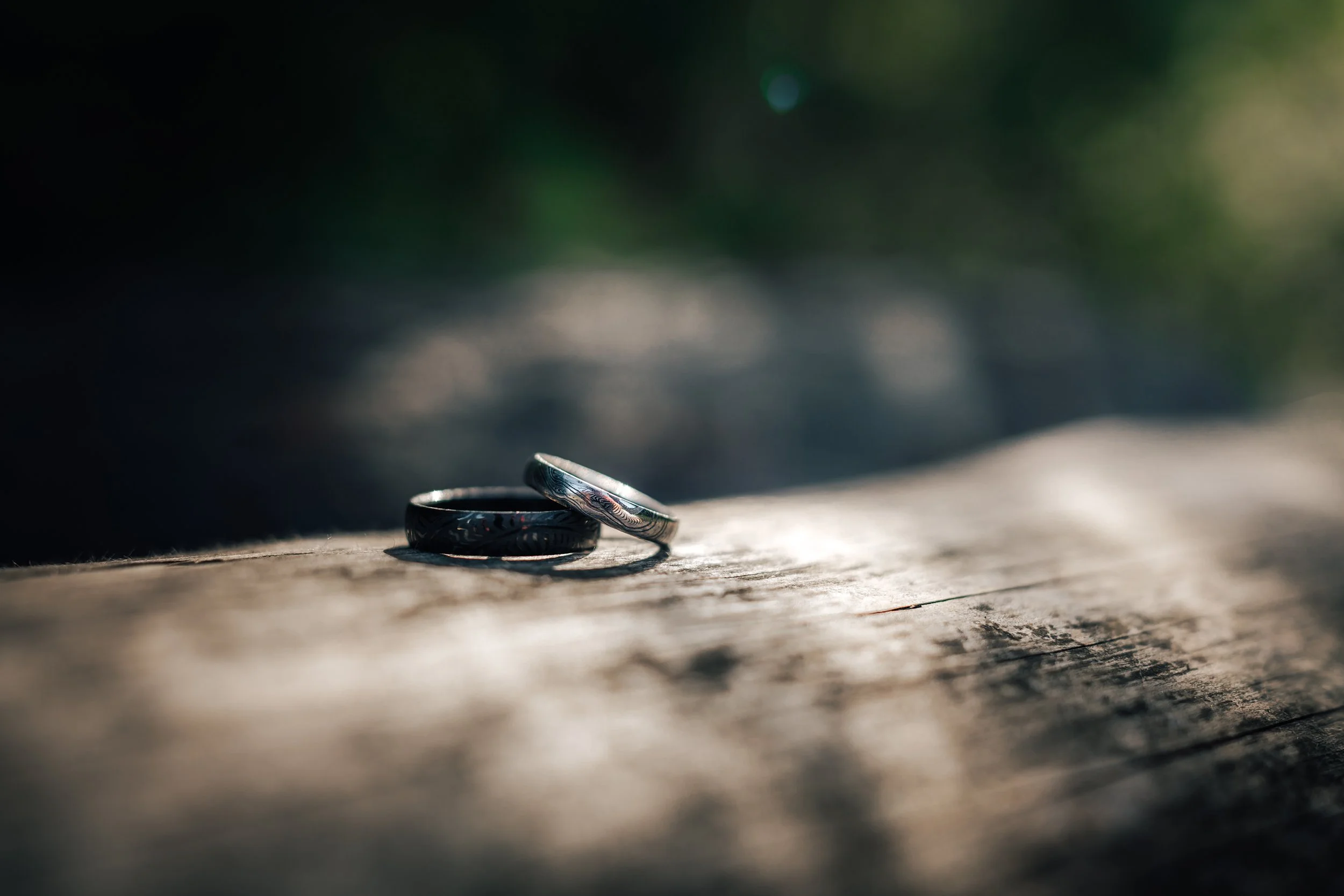 Two wedding rings placed on a rustic wooden surface with blurred green foliage in the background.