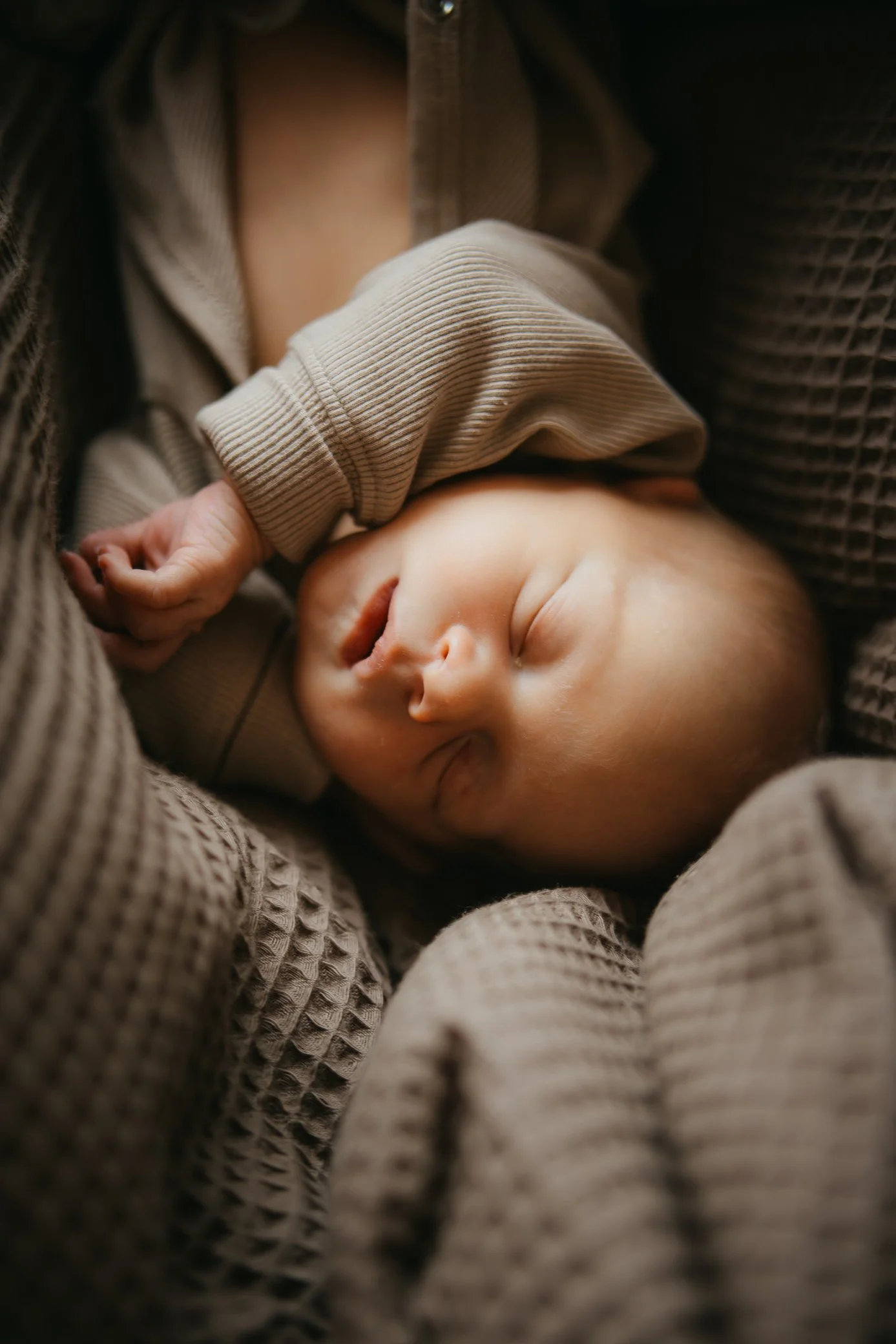 Close-up of a sleeping baby nestled in a brown textured blanket and wearing a beige knit sweater.