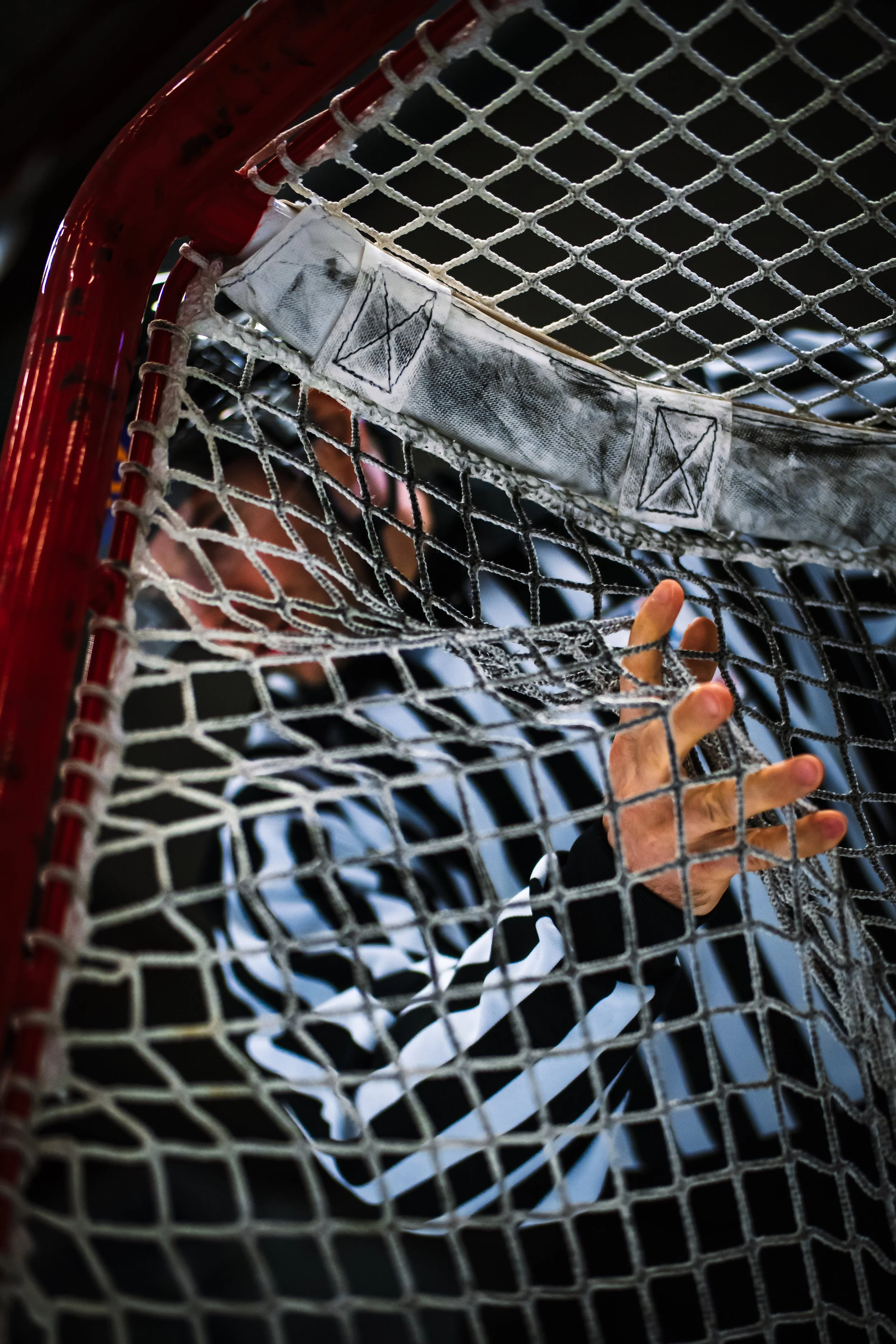 A hockey goalie in black and white jersey reaching through the goal netting.