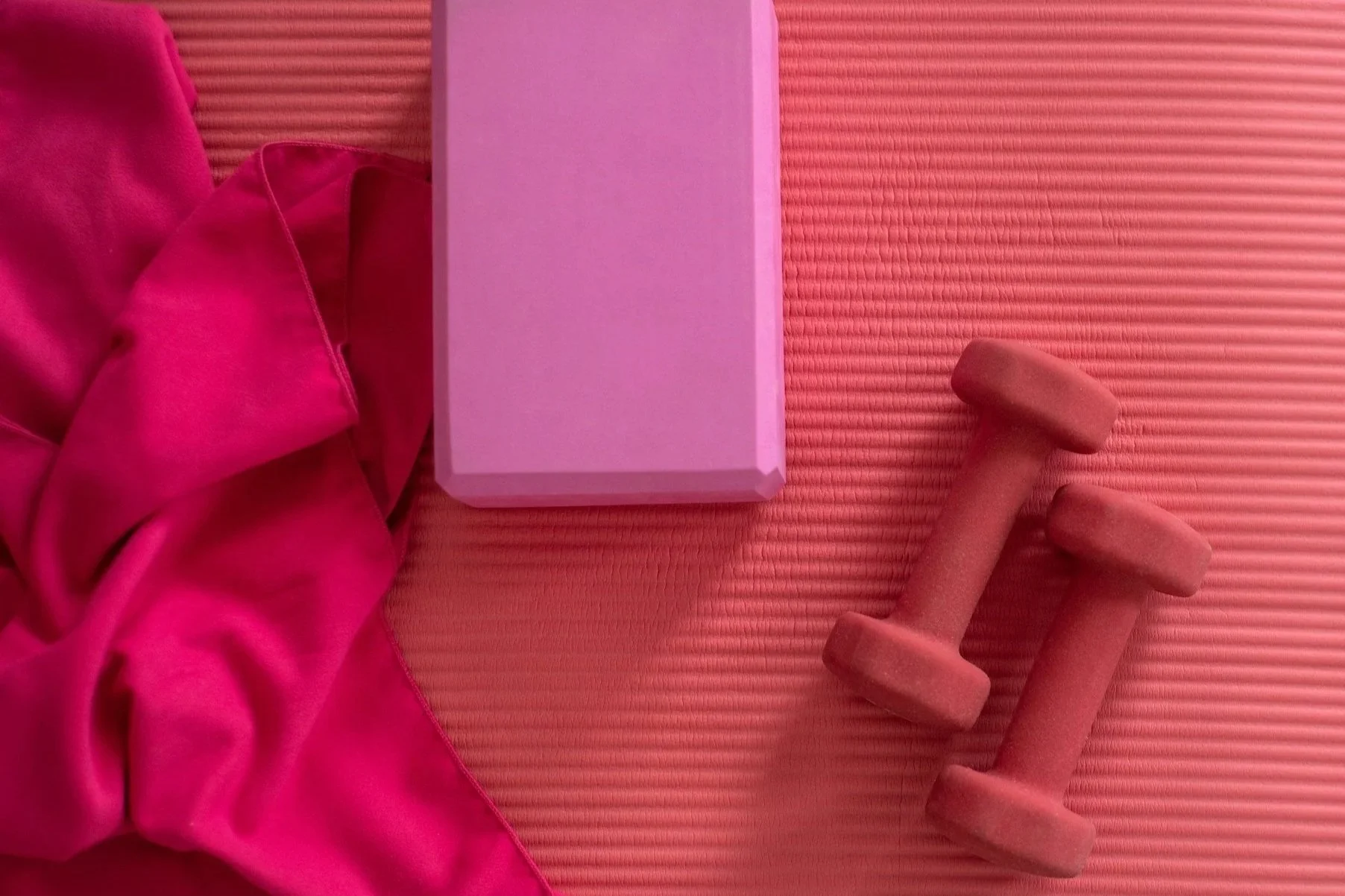 Pink fabric, pink yoga block, pink dumbbells, and pink textured yoga mat.