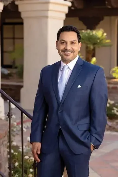 A man in a blue suit standing outdoors in front of a building with white columns, smiling at the camera.