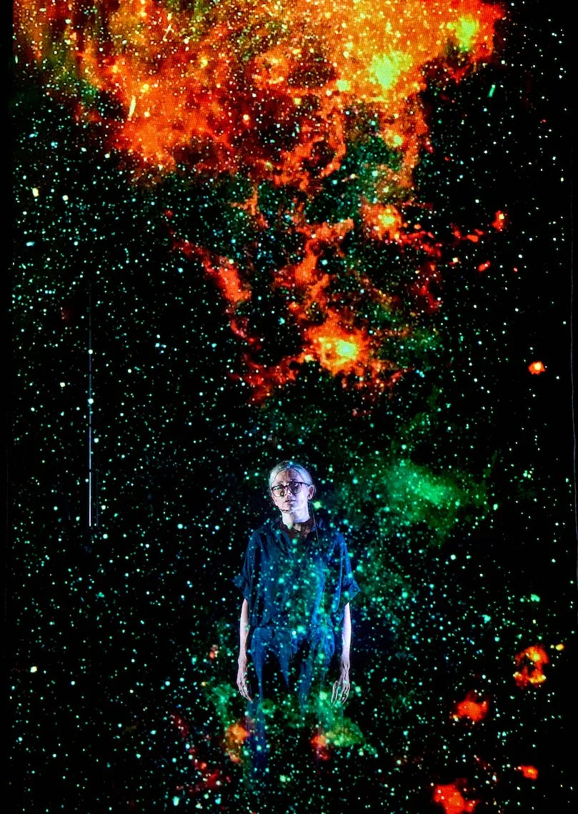 Person standing amidst a backdrop of a colorful, star-filled galaxy with clouds of orange, red, green, and blue