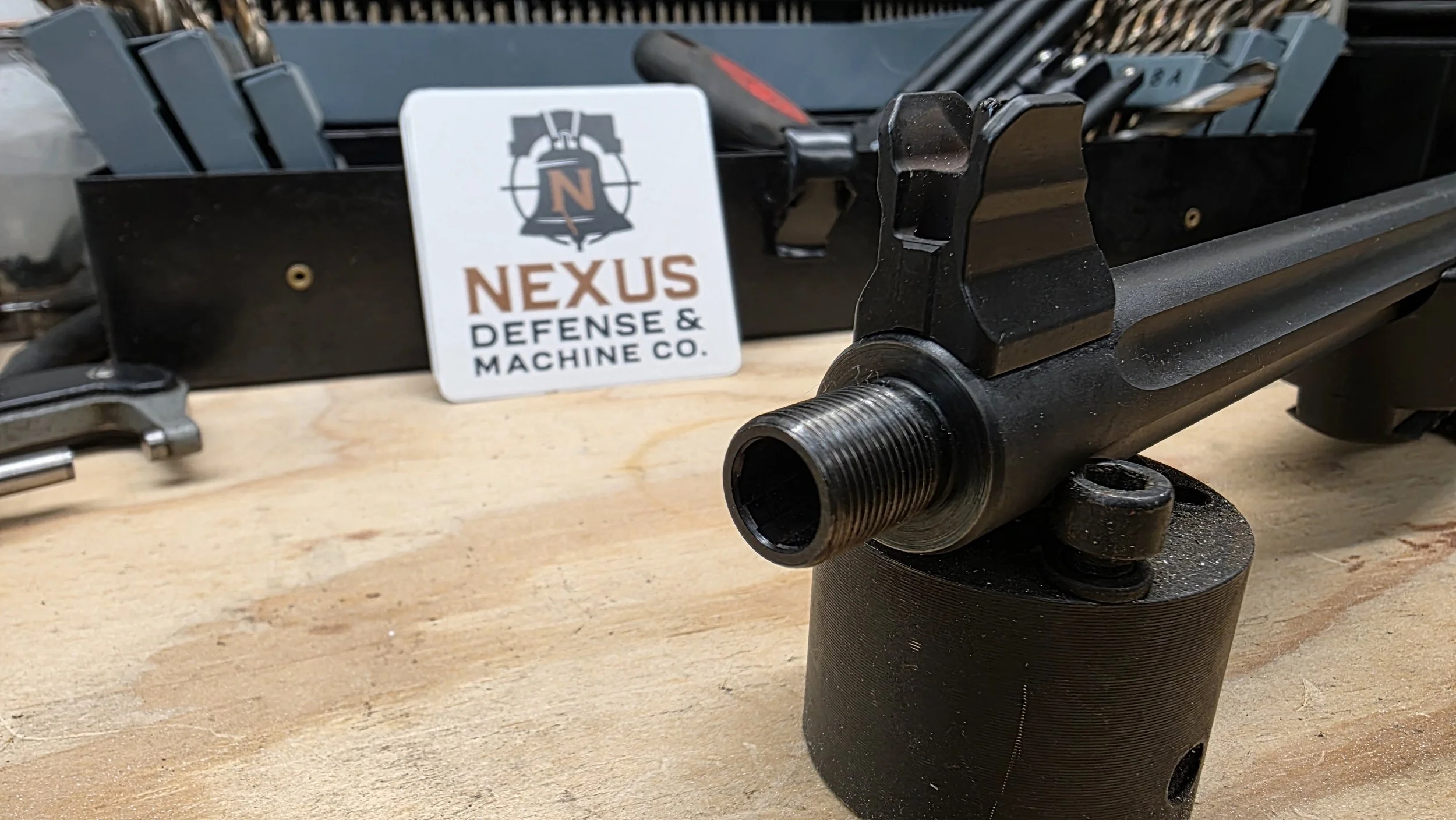 Precision threaded barrel and mount by Nexus Defense & Machine Co with shop branding in background logo sign in the background.