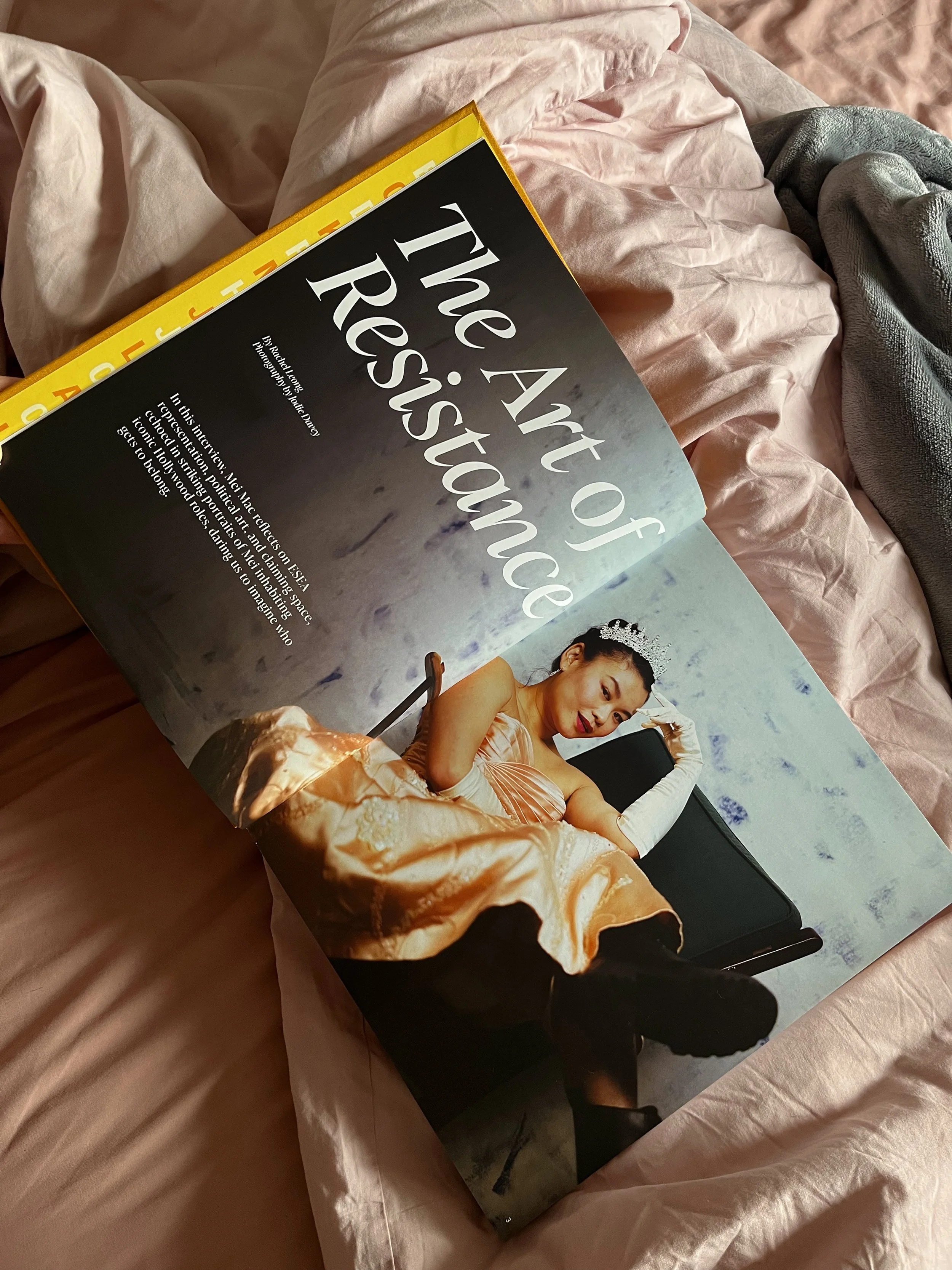 Open magazine on a bed featuring a woman dressed in a peach-colored gown with a tiara, sitting on a black box, with the headline 'The Art of Resistance'.