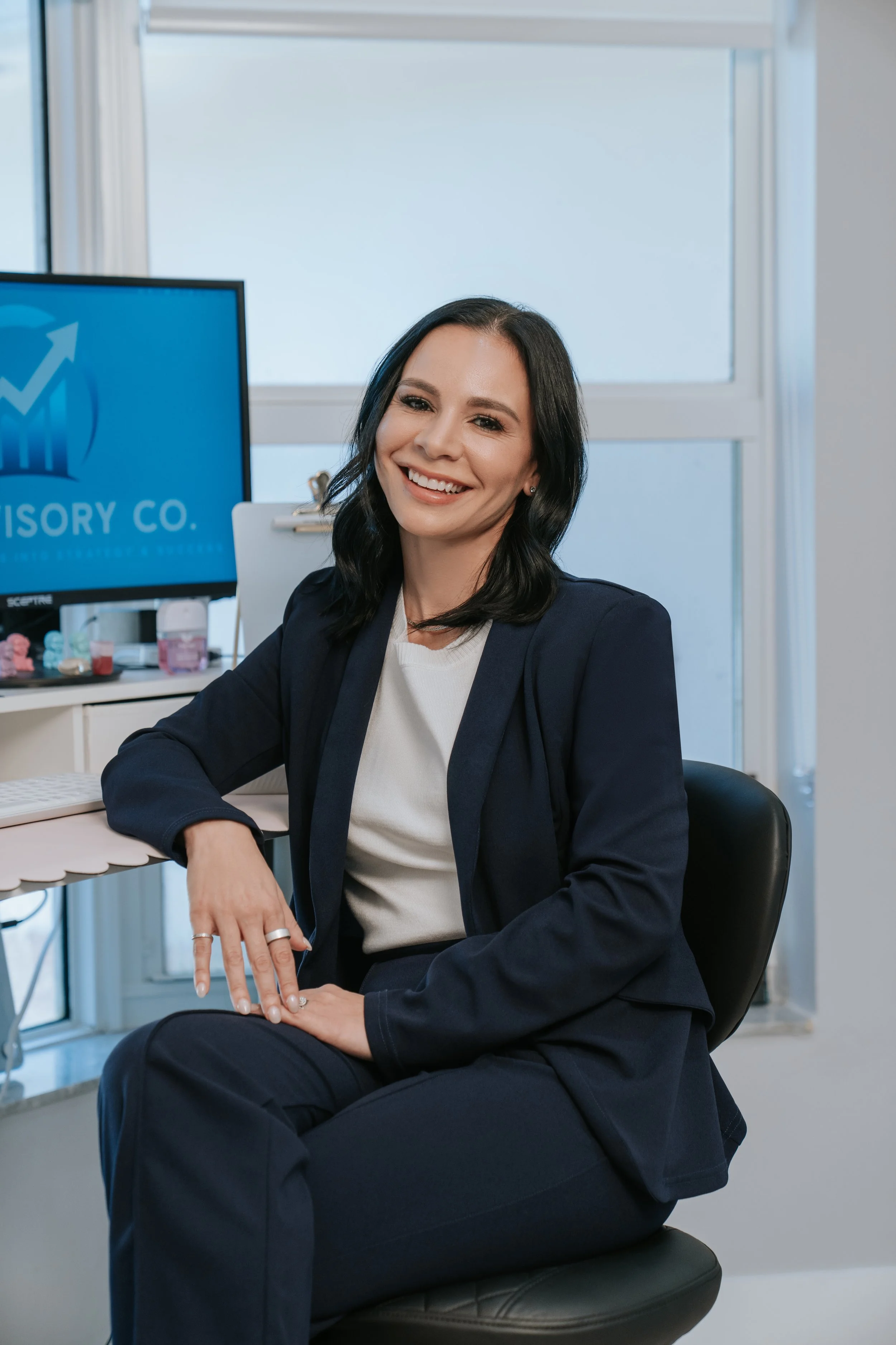 A woman smiling, sitting in an office, with a computer monitor showing a rising graph and the words 'Advisory Co.'