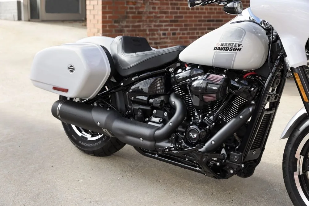 Close-up of a Harley-Davidson motorcycle with a white gas tank, saddle bags, black engine, and exhaust pipes, parked outdoors on a concrete surface.