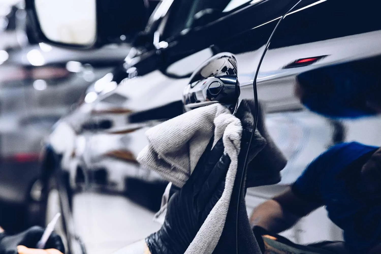 A mechanic cleans the side of a black car with a towel in an auto repair shop.