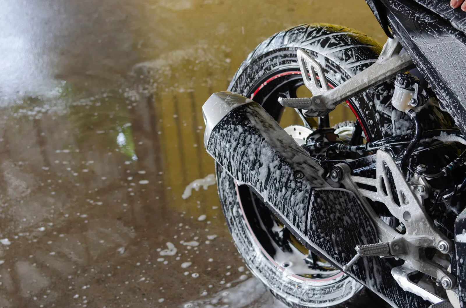 Close-up of a motorcycle tire and front fender covered in soap suds, with a muddy ground in the background.