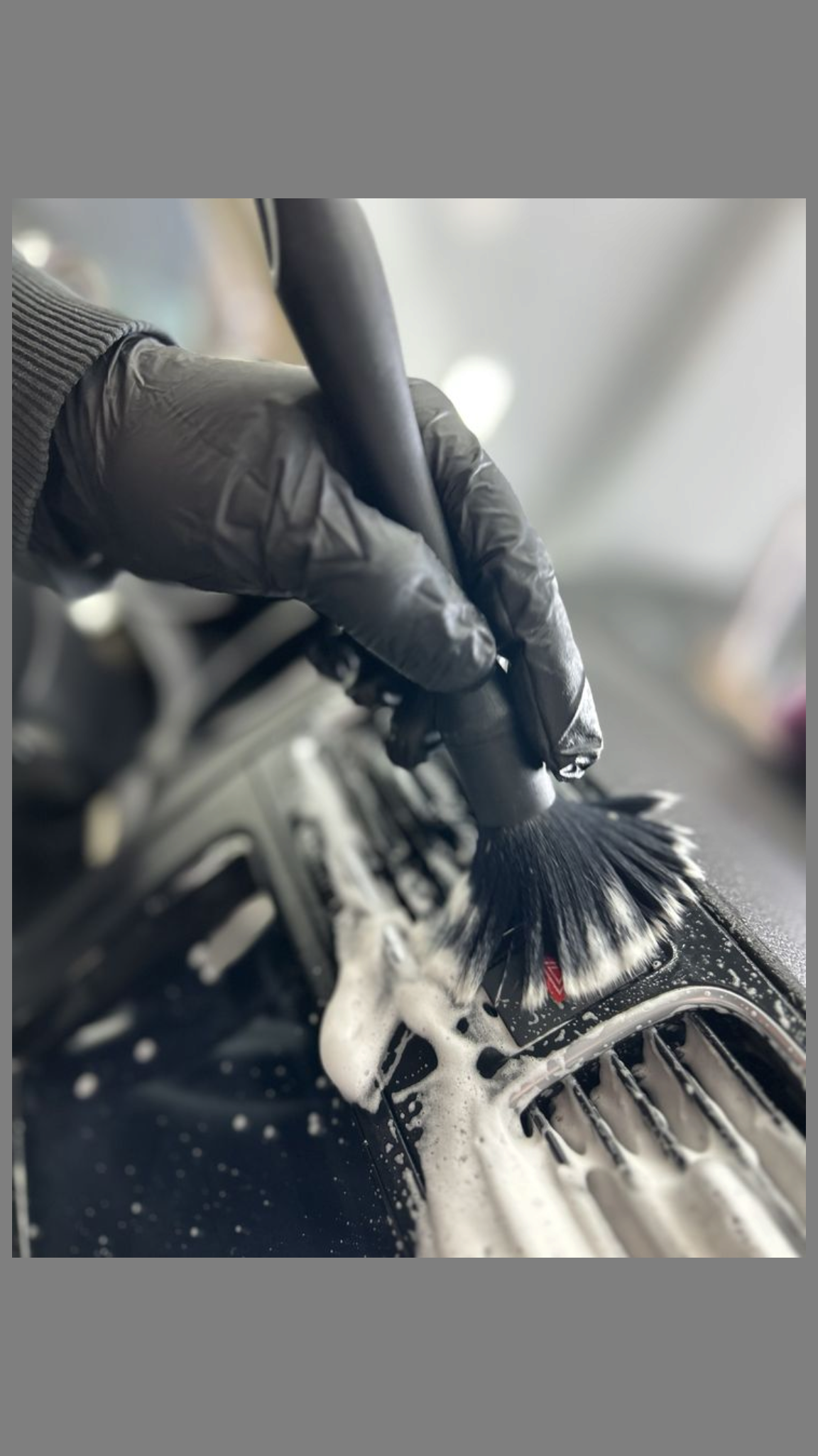 Close-up of a person wearing black gloves cleaning a motorcycle with a brush and soap suds.