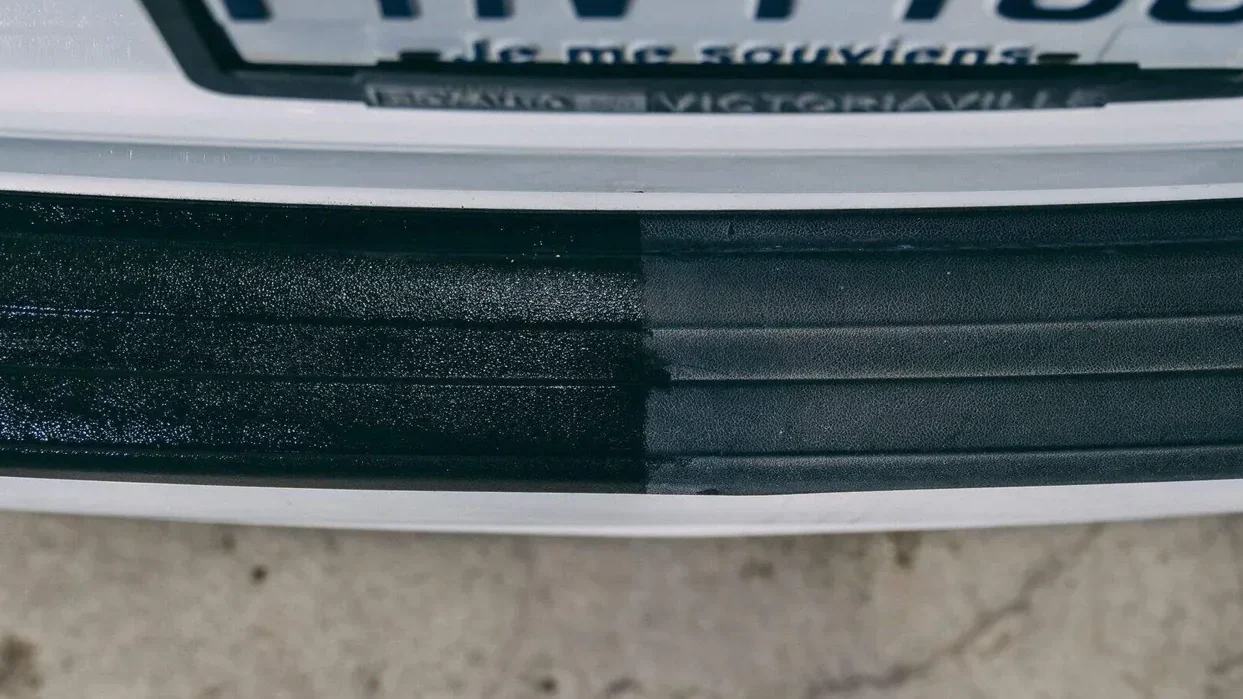 Close-up of black tire sidewall on a white rim, with part of a vehicle license plate visible in the background.