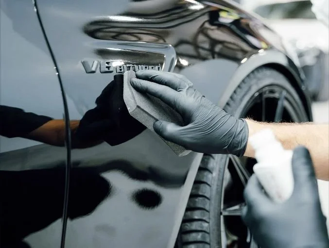 Person polishing a black car with a cloth, focusing on the side emblem that says 'V8 BiTurbo'.