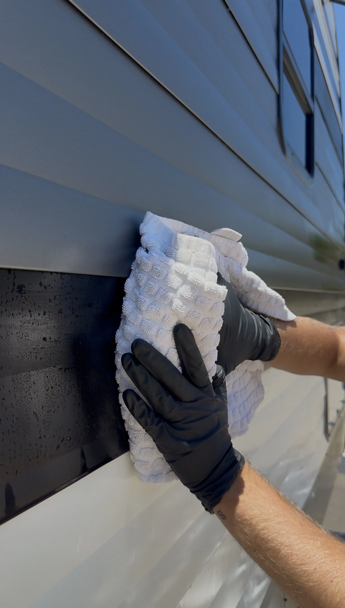 Person wearing black gloves cleaning or polishing a window or glass surface with a white cloth.