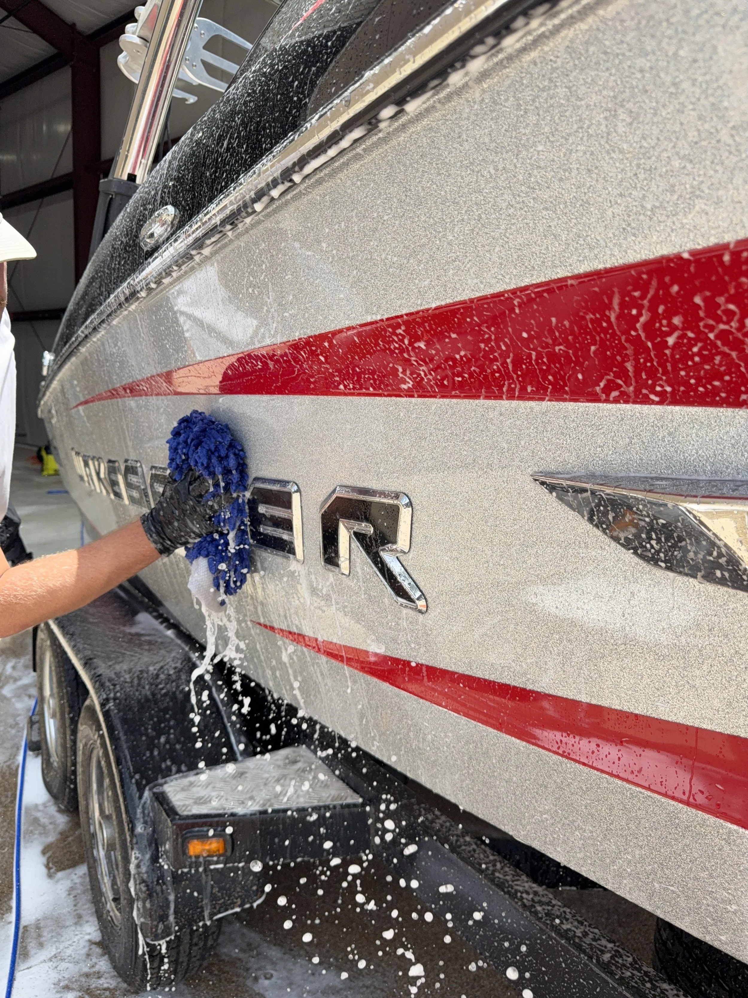A person washing and rinsing a black and gray camper with soap and water, using a blue sponge, at an indoor facility.