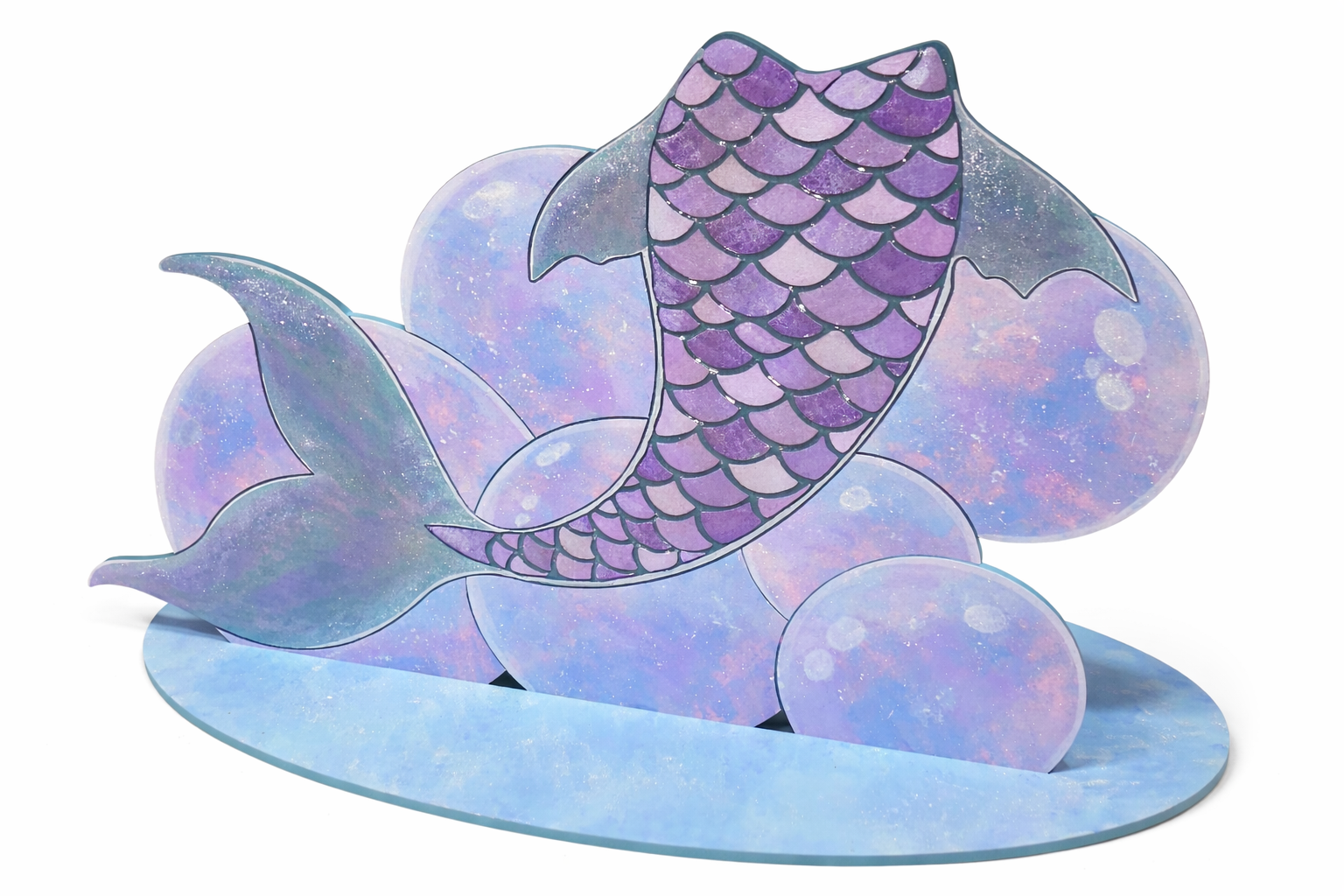 Decorative paper craft of a purple mermaid tail with scalloped scales resting on pastel-colored, galaxy-patterned spheres and a water-shaped base.