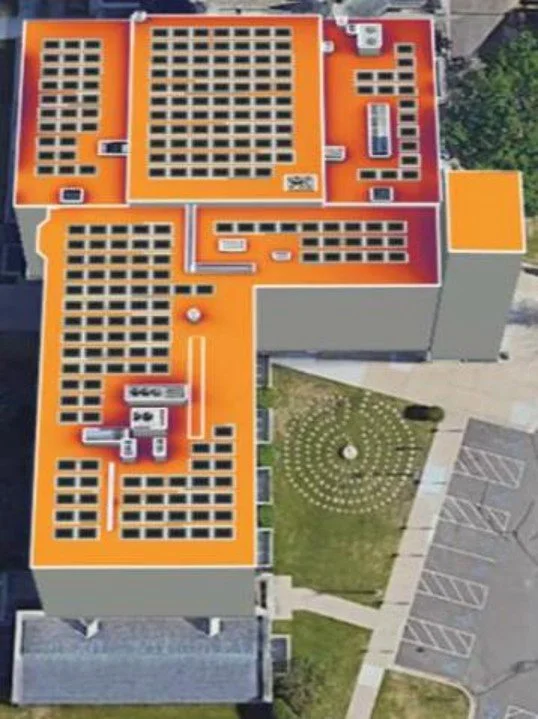 Aerial view of a building with a bright orange roof featuring numerous solar panels, alongside a landscaped area with a circular pattern and parking lot.