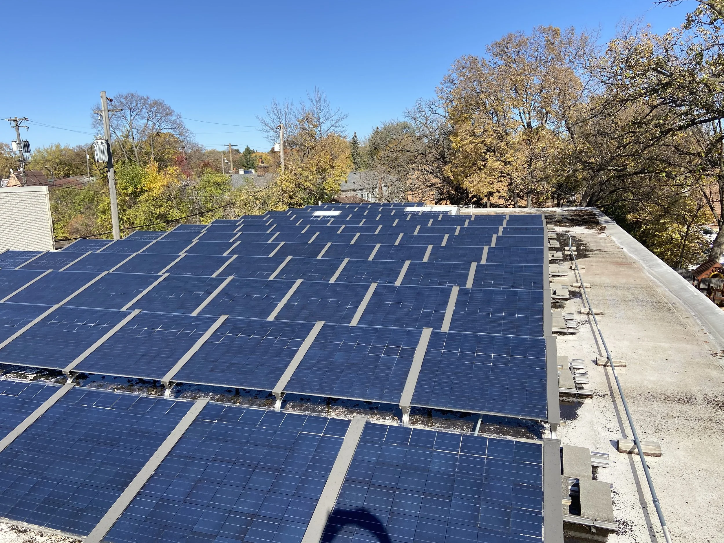 Roof with solar panels and a clear blue sky, with trees in autumn colors in the background.