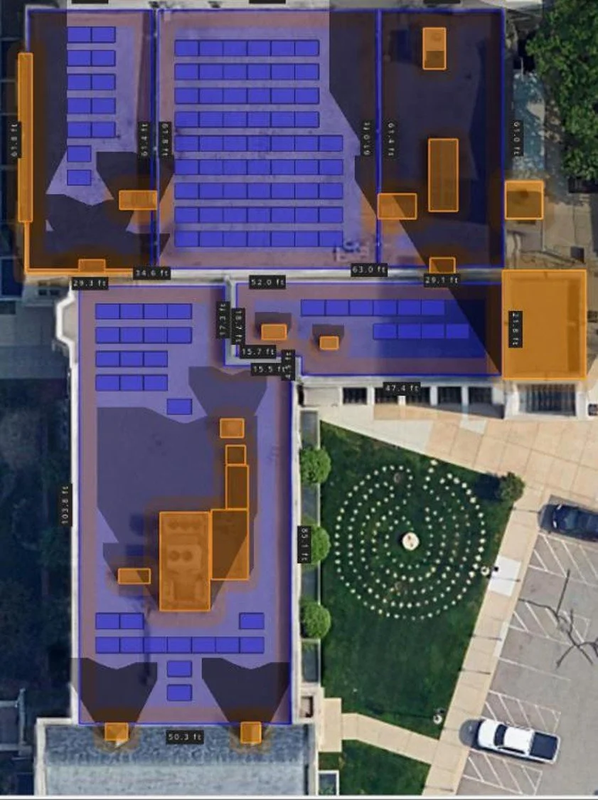 Top-down view of a building with marked measurements, solar panels on the roof, and surrounding outdoor area with a circular patterned landscaping.