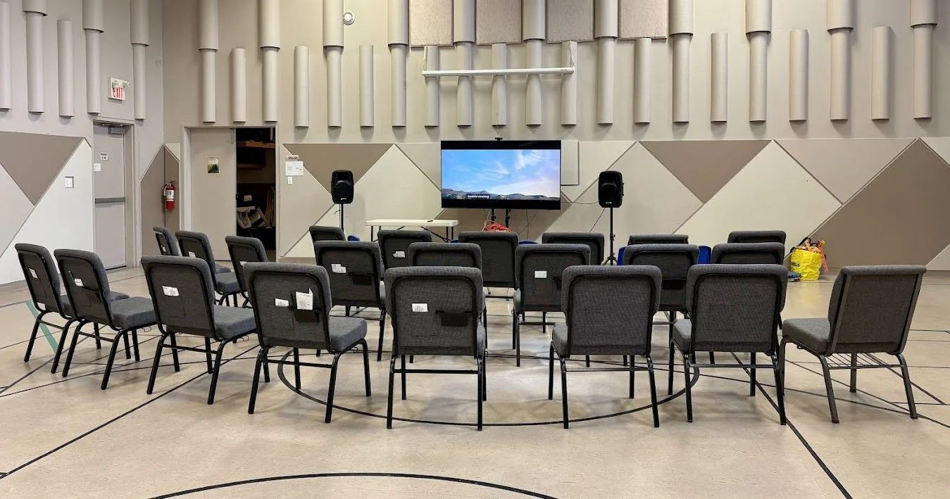 An empty conference or presentation room with chairs arranged in rows facing a screen with two speakers on stand on either side.
