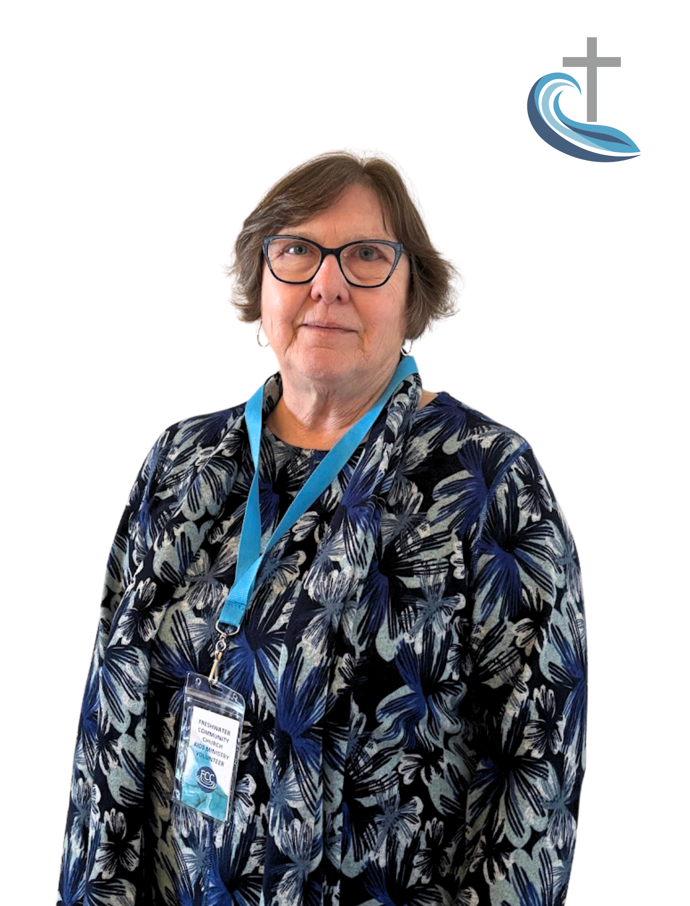 A woman wearing glasses, a black and blue patterned blouse, and a conference badge with a blue lanyard, standing against a white background with a stylized wave and cross logo in the top right corner.